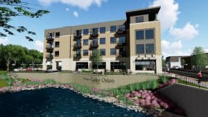 Modern apartment building with lakefront view in Lake Orion, featuring contemporary architecture, outdoor seating, and lush landscaping.