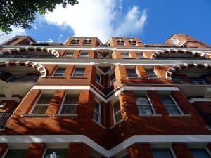 Modern brick apartment building with ornate architectural details and balconies, viewed from below against a bright blue sky, showcasing Rochester property management and rental opportunities.