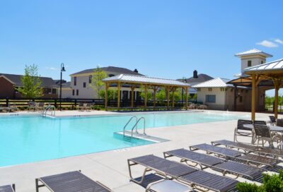 Modern outdoor swimming pool at Rochester Property Management Group community with sun loungers, shaded pavilions, and landscaped surroundings for residents’ leisure.